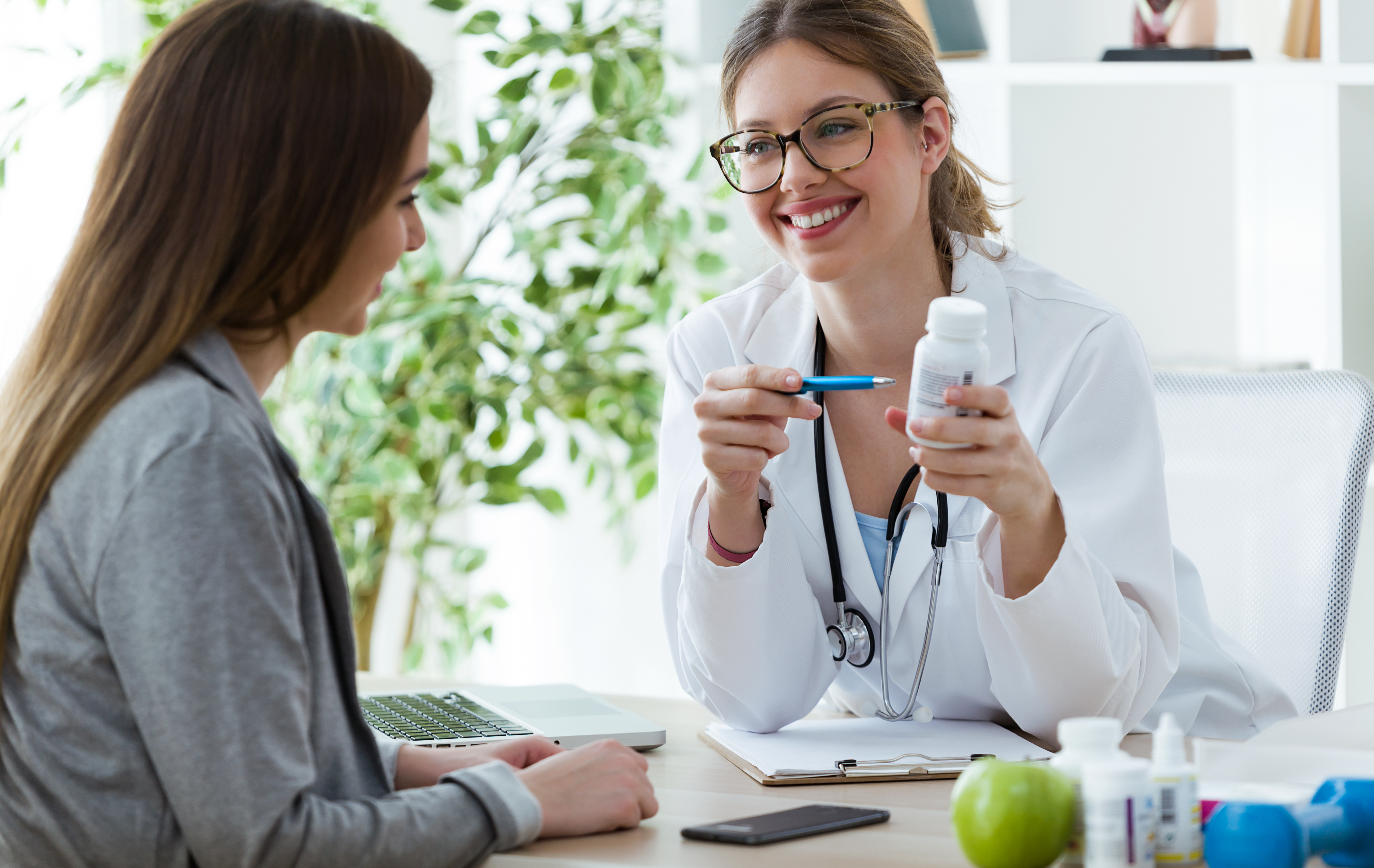 An image showcases a friendly and knowledgeable doctor engaged in a conversation with a female patient at a desk. Both the doctor and the patient are smiling, indicating a positive and supportive environment. The desk is adorned with various supplements and paperwork, suggesting a comprehensive approach to hair loss treatment. The image reflects the hormone replacement therapy clinic's commitment to personalized care, as the doctor discusses available treatment options tailored to the patient's specific needs. It conveys a sense of collaboration, expertise, and a shared goal of addressing female hair loss and restoring confidence in patients.